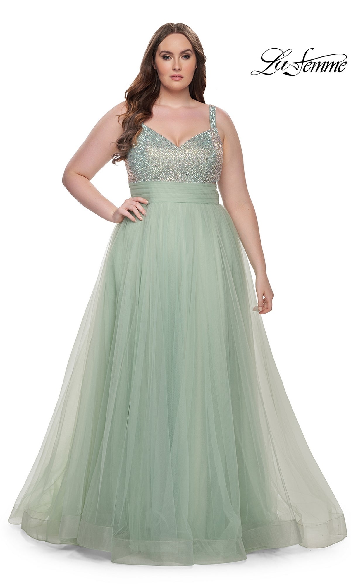 A woman wears the La Femme Long Prom Dress 31251, a plus-size gown in light green with a sparkling beaded bodice and tulle skirt, standing against a white background.